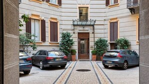 Un patio con dos coches aparcados a ambos lados, una entrada central con una puerta y plantas en macetas.