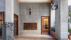 Un vestíbulo con pared de piedra, puerta de madera, barandilla metálica y una planta en maceta.