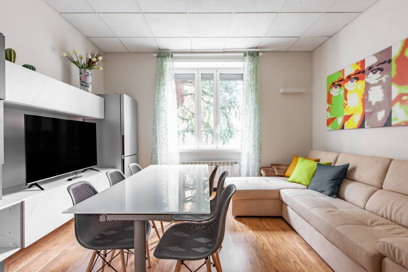 A modern living room with a dining area, a flat-screen TV, and a sofa with cushions.