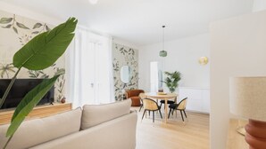 A modern living room with a sofa, a dining table with chairs, a TV, and a large plant.