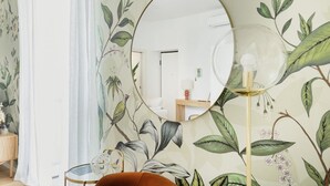 A room with a floral wallpaper, a round mirror, and a modern lamp.