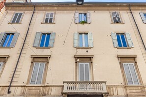 Ein mehrstöckiges Gebäude mit gleichmäßig verteilten Fenstern, einem zentralen Balkon und einer sichtbaren Stromleitung.