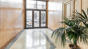 A hallway with a polished floor, a large glass door with metal bars, and a potted plant. - Easylife - Luxury and Comfort in Brera district (Milano)