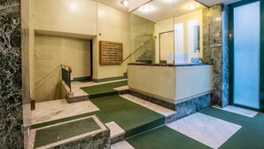 A hotel lobby with a marble reception desk, a staircase with green carpeted steps, and a glass door leading to another area. - Easylife-Spacious and comfortable apartment in the Duomo (Milano)