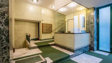 Eine Hotelhalle mit einem Marmor-Rezeptionsschalter, einer Treppe mit grünem Teppich und einer Glastür zu einem weiteren Bereich.