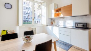 A modern kitchen with white cabinets, a microwave, and a window overlooking a cityscape. - Easylife-Spacious and comfortable apartment in the Duomo (Milano)