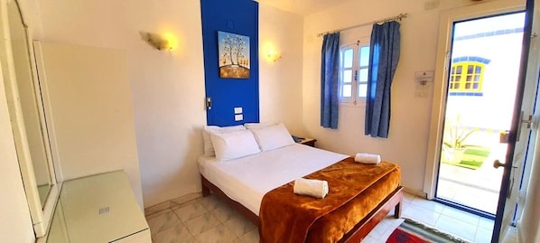 A bedroom with a bed, a blue wall, a window with curtains, and a door leading outside. - Neptune Dahab Hotel (Dahab)