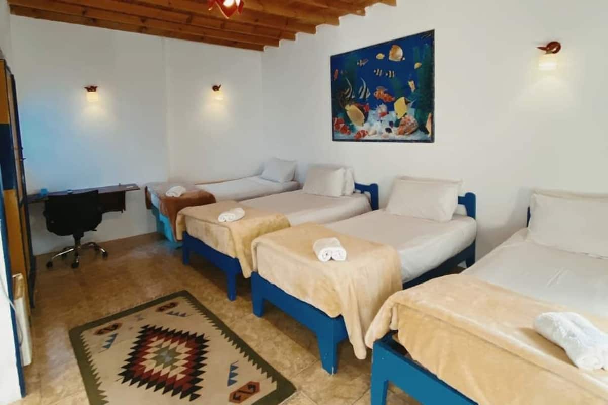 A room with three beds, a desk, and a painting.