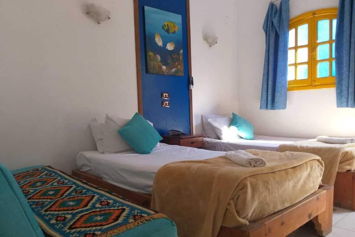 A room with two beds, a sofa, and a window with curtains.