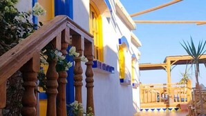 A building with a blue and white facade, a wooden staircase with a balustrade, and a tiled patio area. - Neptune Dahab Hotel (Dahab)