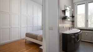 Ein Schlafzimmer mit Bett, einem weißen Kleiderschrank, einem Badezimmer mit Waschbecken und Spiegel sowie einem Fenster mit Blick.