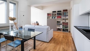 Ein zeitgemäßer Wohnraum mit einem Glastisch, einem grauen Sofa und einem Bücherregal voller Bücher.