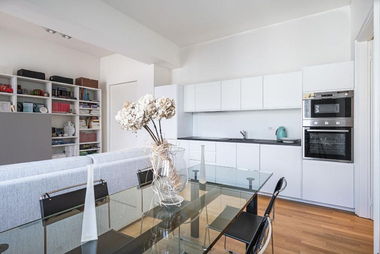A modern kitchen with white cabinets, a glass dining table, and a built-in oven.