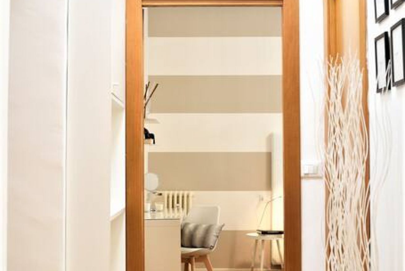 Quarto moderno com porta de madeira, uma cadeira, uma pequena mesa e uma planta decorativa.