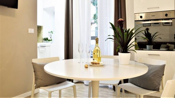 A modern kitchen with white cabinets, a built-in oven, and a dining area with a round table and four chairs.