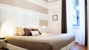 A bedroom with a large bed, a bedside table, a lamp, and a window with curtains.
