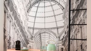 A room with a large mural of an ornate building's interior, a pink cabinet with a coffee maker and teapot, and a glass of water. - Amazing apartment in Duomo by Easylife (Milano)