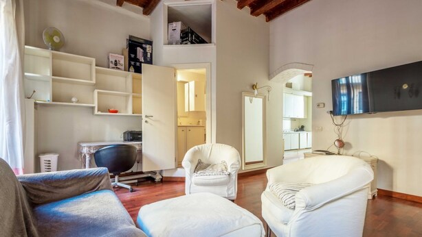 Un salon spacieux avec un plafond haut, des fauteuils blancs, un canapé et un téléviseur fixé au mur.