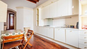 Une cuisine avec des meubles blancs, une table à manger en bois avec des chaises, et une porte visible qui donne sur une autre pièce.