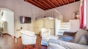 Un salon chaleureux avec un plafond en bois, un canapé blanc, un canapé gris, un fauteuil blanc et un meuble blanc sur lequel est fixé un téléviseur.