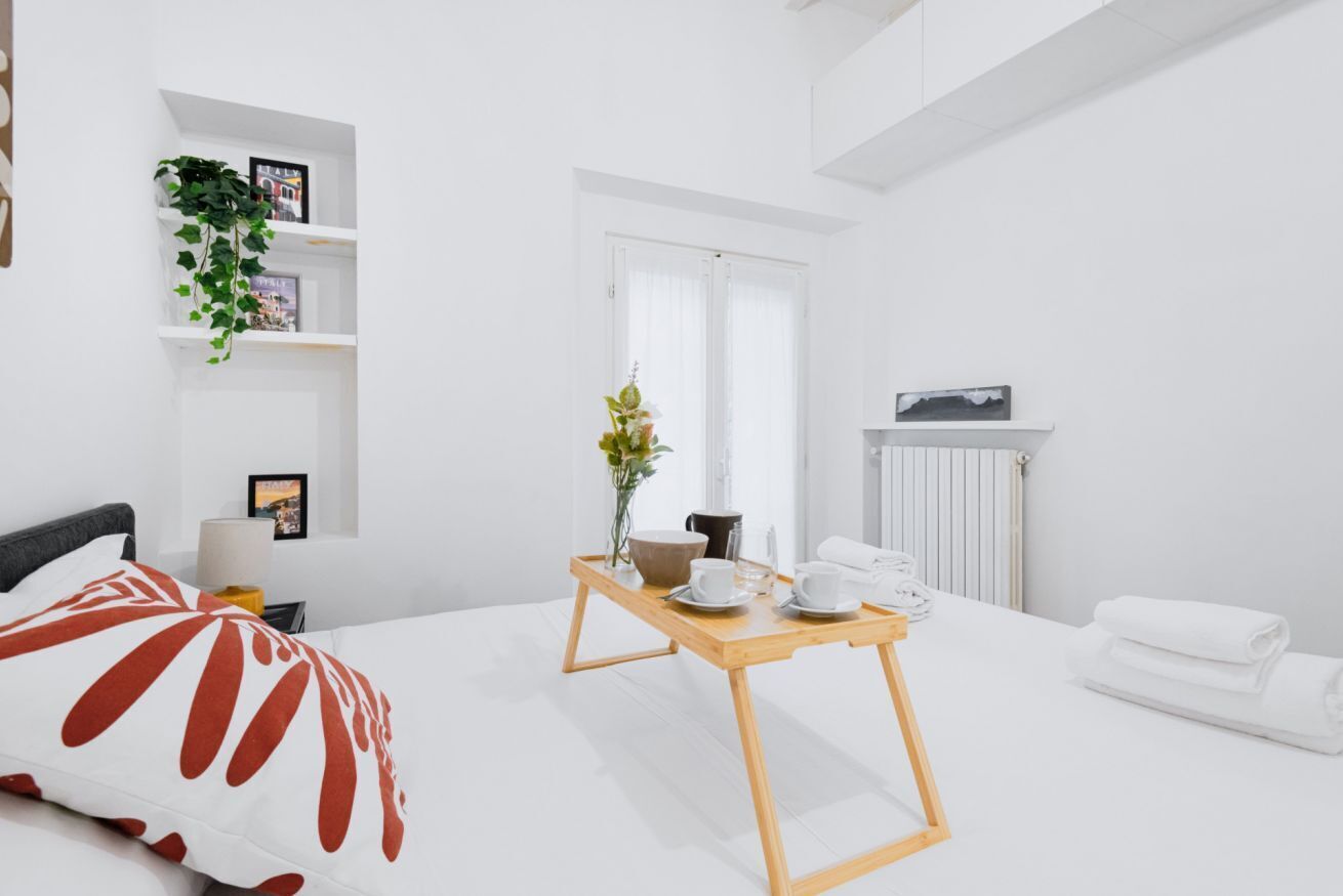Ein modernes, minimalistisches Schlafzimmer mit Bett, Nachttisch und kleinem Fenster.