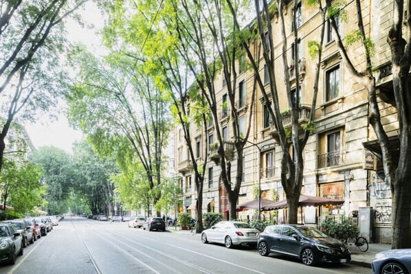 A tree-lined street with parked cars and a tram line.