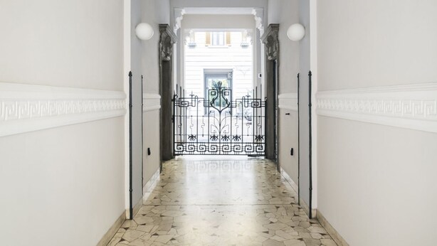 A hallway with a patterned floor leading to a door with a decorative metal gate.