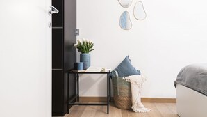 A room with a bed, a small table with a plant, a basket, and wall art.