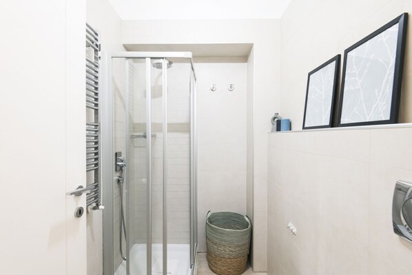 A modern bathroom with a glass shower enclosure, a towel rack, and a waste basket.