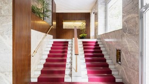 A grand staircase with red carpeted steps, wooden paneling, and a modern light fixture. - Easylife - Classy abode in the Conciliazione area (Milano)