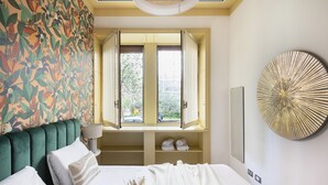 A bedroom with a large bed, a window with open shutters, a wall with a tropical print, and a round decorative piece on the wall. - Easylife - Classy abode in the Conciliazione area (Milano)