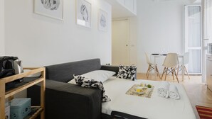 Een moderne hotelkamer met een bed, een bureau en een stoel. Er hangen ingelijste foto’s aan de muur en staat een klein plantje op het bureau.