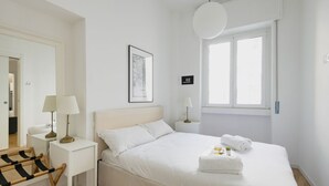 Een minimalistische slaapkamer met een groot bed, nachtkastjes, een hanglamp en een raam.