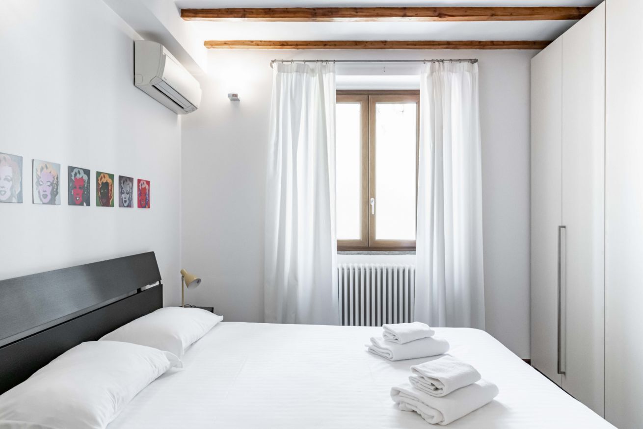 A modern hotel room with a large bed, white linens, a window with curtains, and artwork on the wall.