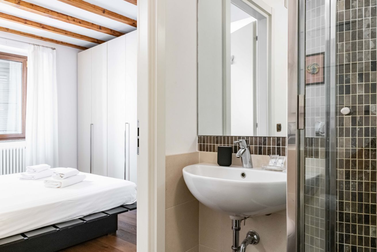 Ein Schlafzimmer mit einem Bett, einem weißen Waschbecken und einer Duschkabine aus Glas.