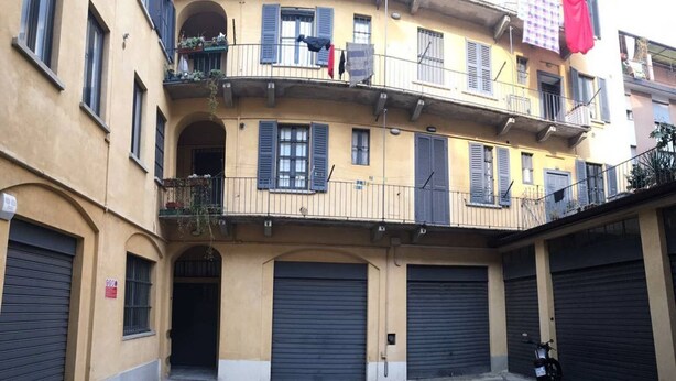 A multi-story building with closed shutters, balconies with plants, and a motorcycle parked in front. - Easylife - Stunning apt in the design district (Milano)