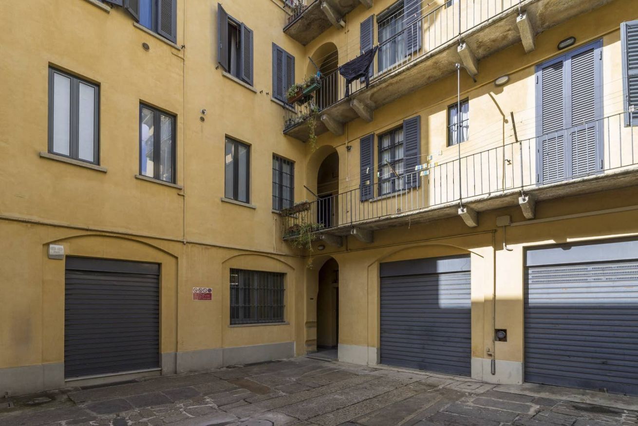 Ein gelbes Gebäude mit drei Garagentoren und einem kleinen Balkon mit Pflanzen.