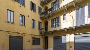 A yellow building with three garage doors and a small balcony with plants. - Easylife - Stunning apt in the design district (Milano)