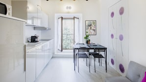 Une cuisine compacte avec un coin repas, un balcon offrant une vue agréable et une porte ornée de motifs floraux violets.
