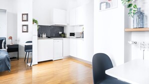 A modern kitchen with white cabinets, a black and white backsplash, and a microwave. There is a dining table with chairs, a small plant, and a shelf with decorative items. - Classic Studio in Washington area by Easylife (Milano)
