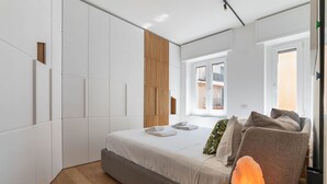 Une chambre moderne avec un lit, une table de chevet en bois, une lampe de sel et une fenêtre donnant sur des immeubles.
