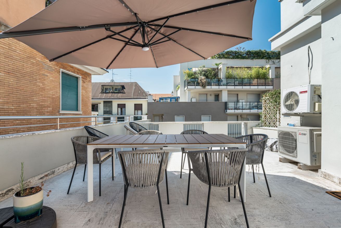 Una terraza en la azotea con mesa y sillas, una sombrilla y unidades de aire acondicionado.