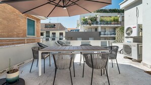 Une terrasse sur le toit, avec une table et des chaises, un parasol et des unités de climatisation.