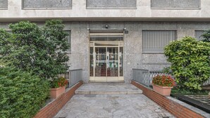 Une entrée d’immeuble avec une porte en verre, un chemin pavé de pierres et des plantes en pot de chaque côté.