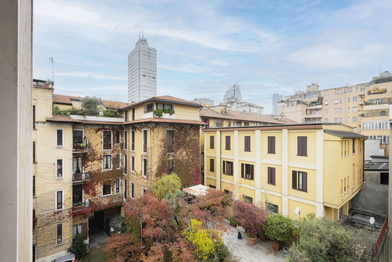A multi-story residential building with balconies, a courtyard with trees, and a modern high-rise in the background.