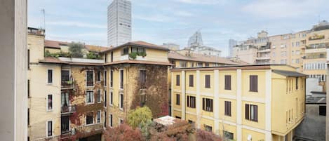A multi-story residential building with balconies, a courtyard with trees, and a modern high-rise in the background.