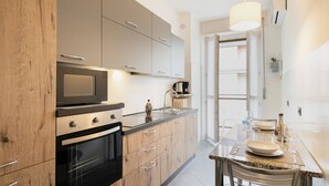 A modern kitchen with wooden cabinets, a built-in oven, a microwave, and a dining area with a table and chairs. - Easylife - Charming flat 5 min from Centrale (Milano)