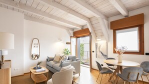 A modern living room with a sofa, chairs, a coffee table, and a dining table. There is a large window and a door leading to an outdoor area. - Easylife - Exclusive penthouse with panoramic view (Milano)