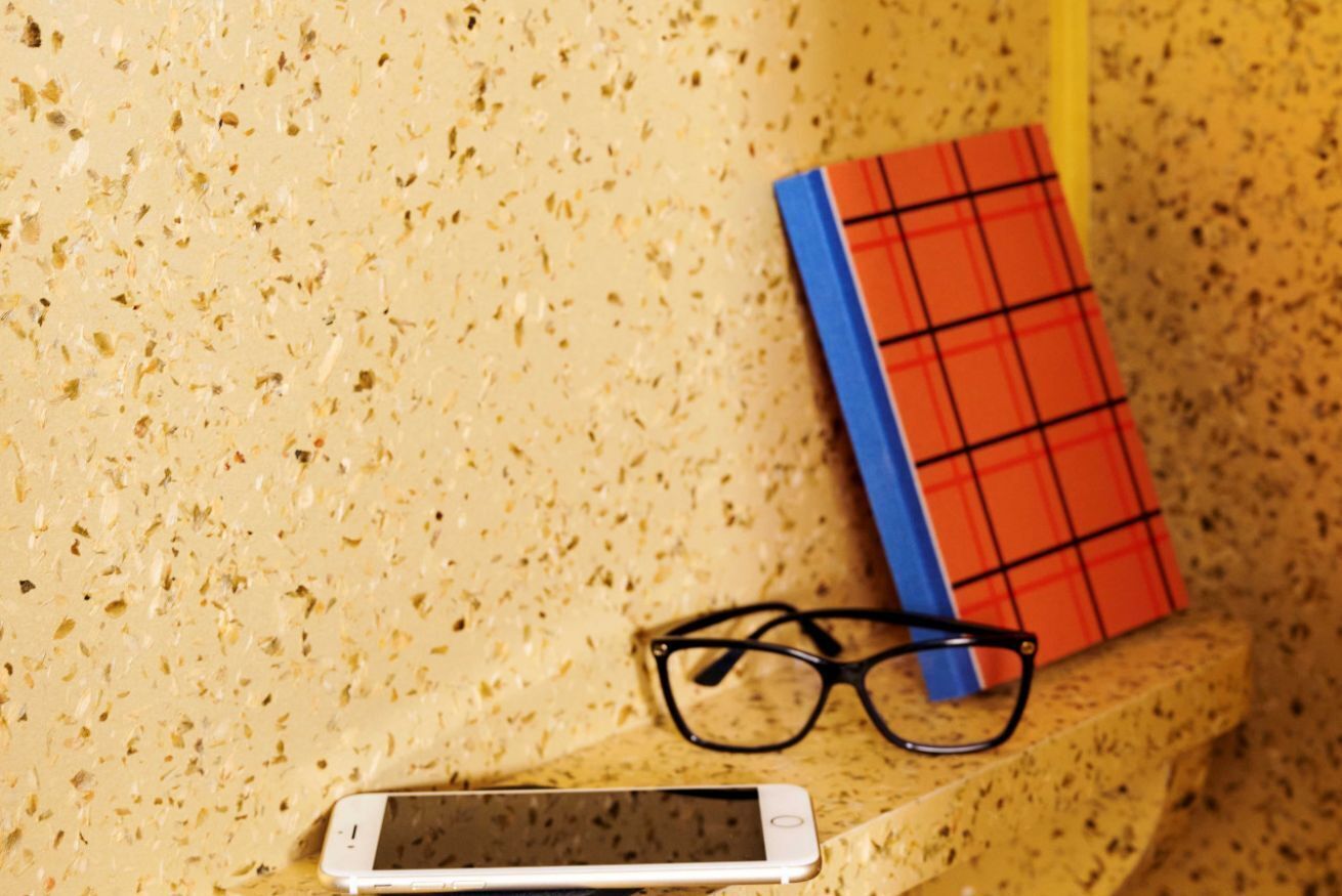 Ein Smartphone, eine Brille und ein rotes und blaues Notizbuch auf einer strukturierten Oberfläche.