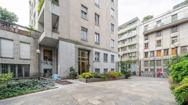 Een binnenplaats met stenen vloeren, een centrale plantenbak met bloemen en een gebouw met meerdere balkons en ramen.